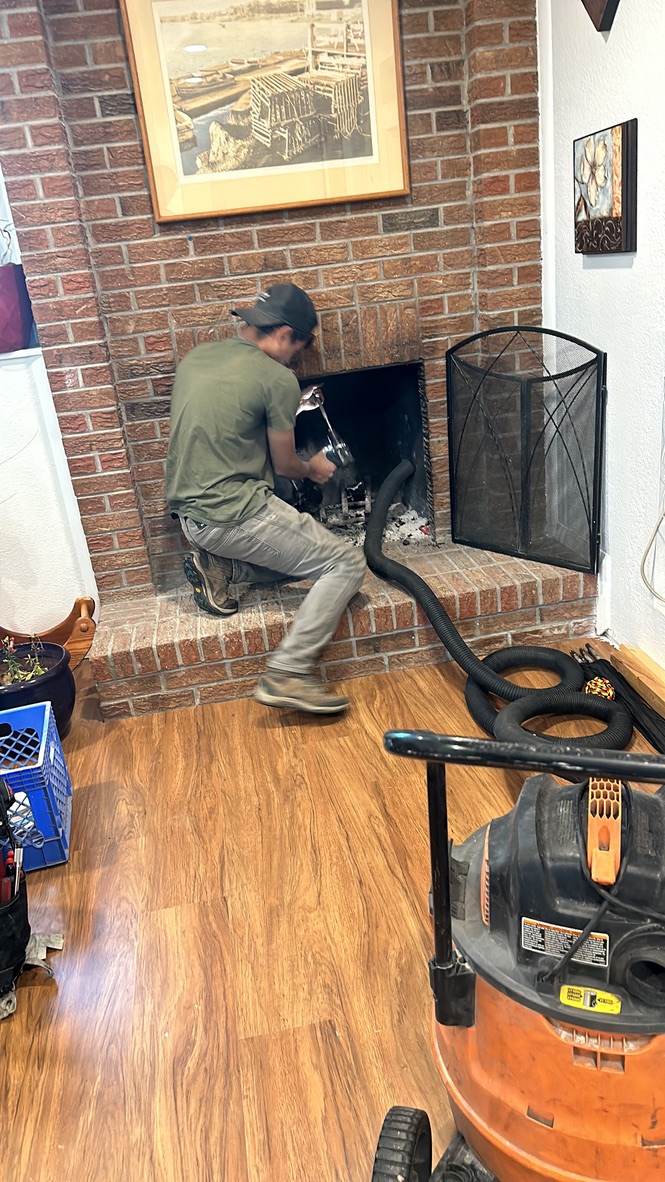 Technician cleaning brick fireplace with professional vacuum equipment